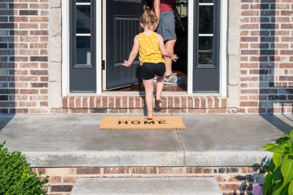 Toddler girl walking in the front door of a brick single family home